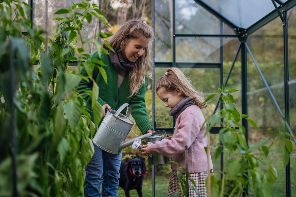 Little,Girl,And,Mother,Watering,Plants,In,Garden,,Using,Collected